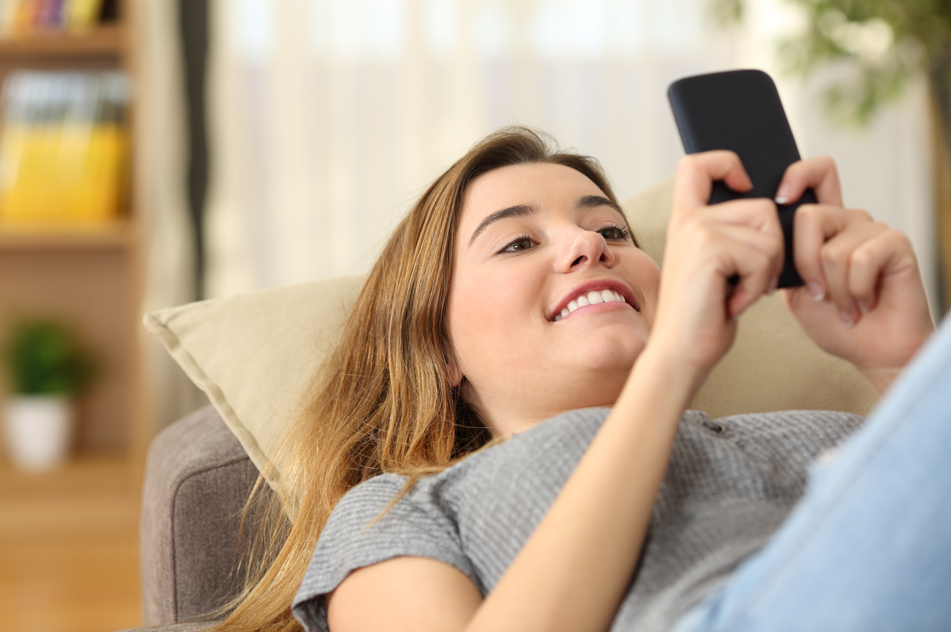 Kvinde ligger i sofaen og kigger glad på sin mobiltelefon