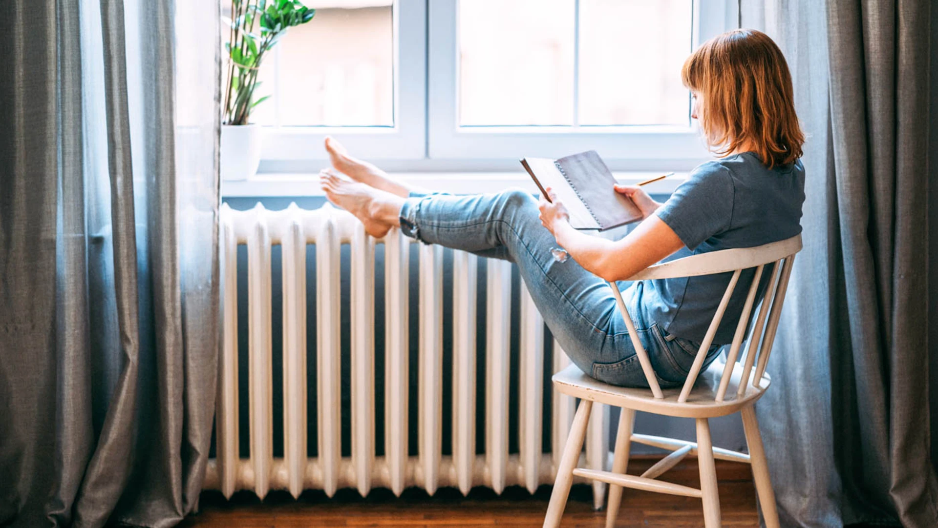 Kvinde sidder på en stol og varmer fødderne på en radiator