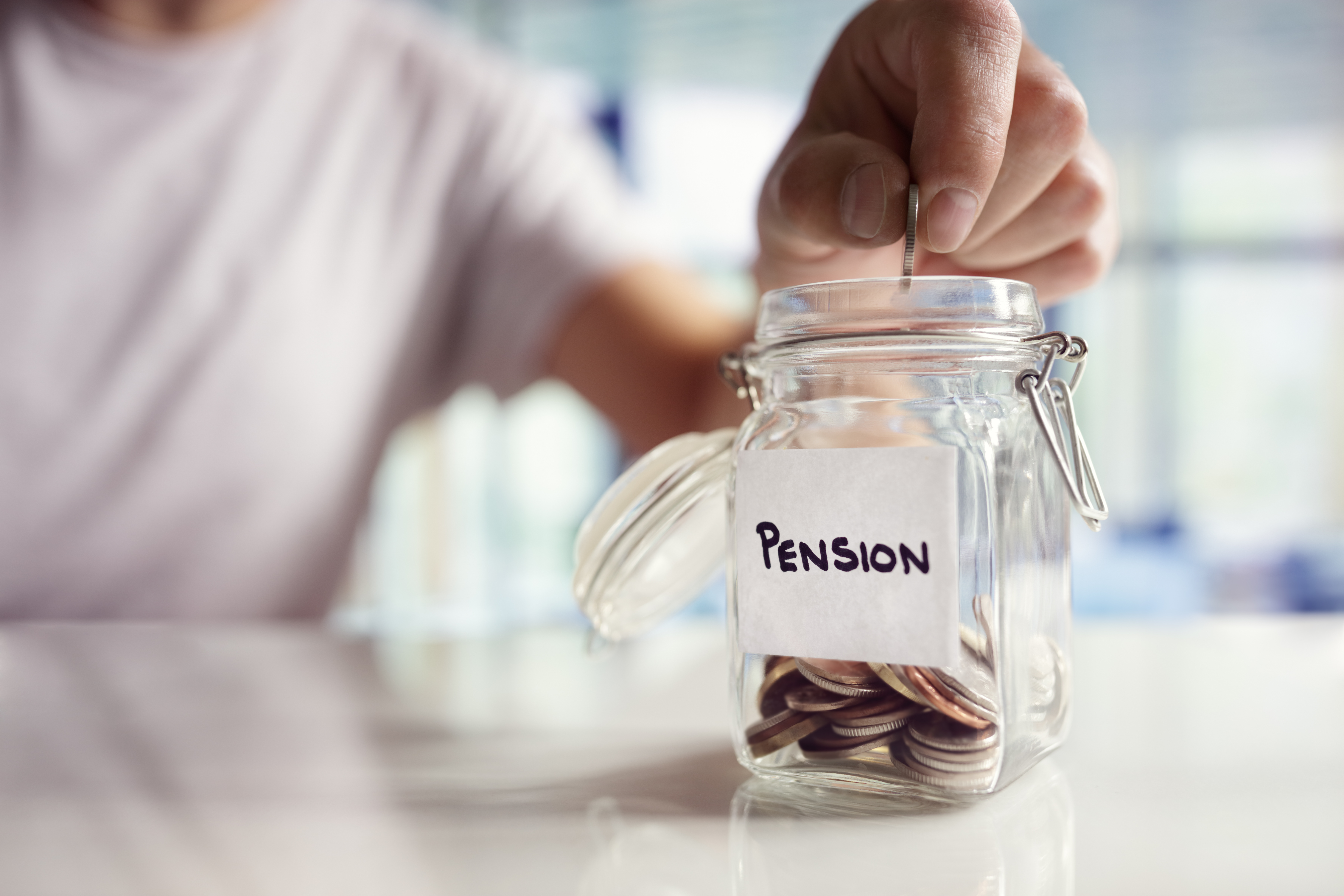 En person putter en mønt i et glas med andre mønter, hvor der står pension på.