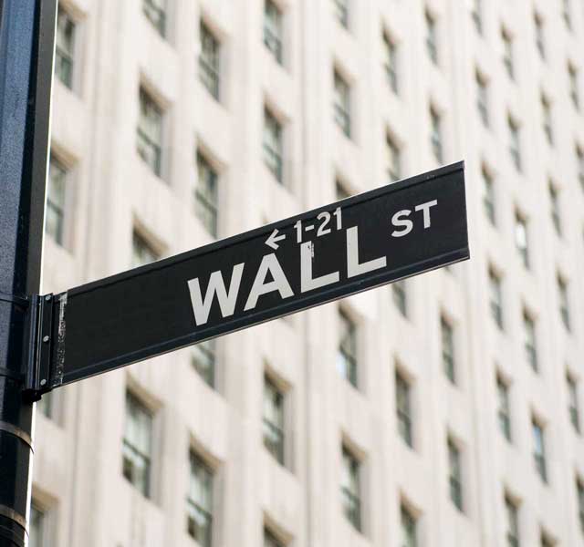 Vejskilt for Wall Street foran en bygning, symboliserer finansverdenens centrum og økonomisk aktivitet.