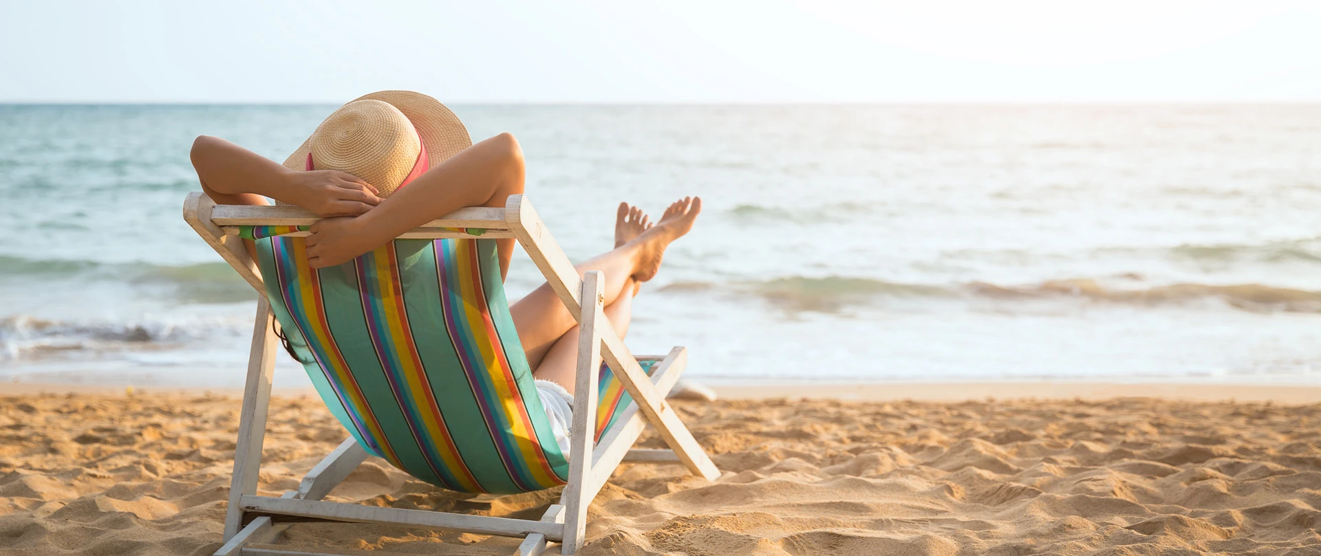Kvinde sidder med solhat på en solstol på en strand.